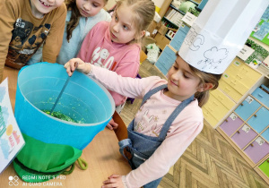 Uczennica klasy 1a w roli kucharki, przygotowującej wiosenną zupę marcową.