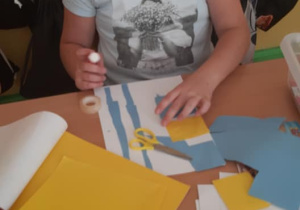 Uczennica nakleja wycięte elementy na karton.