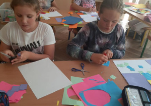 Ucznennice wycinają i naklejają elementy z papieru kolorowego.