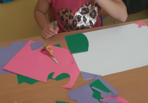 Uczennica wycina i nakleja elementy z papieru kolorowego.