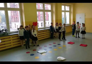 Dzieci stoją przed oknami, na podłodze rozłożone są kolorowe prostokaty.