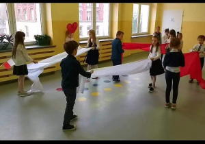 Dzieci trzymają białe i czerwone szarfy.