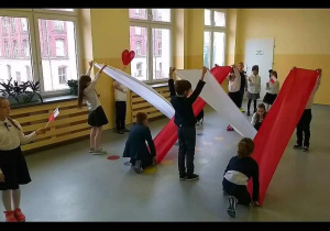 Dzieci trzymają białe i czerwone szarfy.