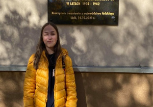 Uczennica klasy 8b stoi przed tablicą pamiątkową dla łódzkich bohaterów walczących o polską edukację.