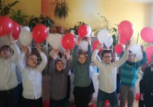 Uczniowie trzymają białe i czerwone balony.