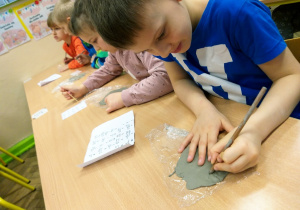 Uczniowie klasy 1a podczas twórczej pracy - pisanie swoich inicjałów paykiem na glinie.