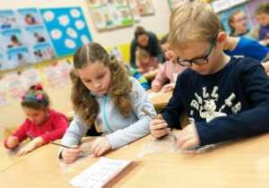 Uczniowie klasy 1a podczas twórczej pracy - pisanie swoich inicjałów patykiem na glinie.